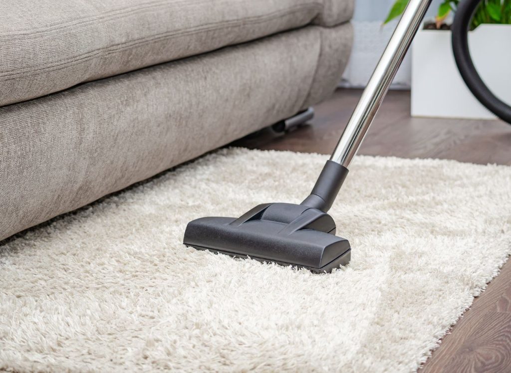 A vacuum cleaner is shown cleaning a white rug, highlighting a carpet cleaning service located in San Antonio, TX.