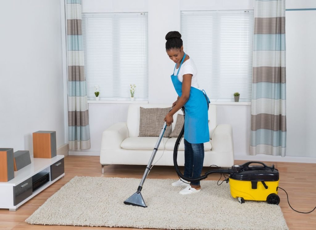 A woman in an apron uses a vacuum to clean a room, highlighting a rug cleaning service in San Antonio, TX.