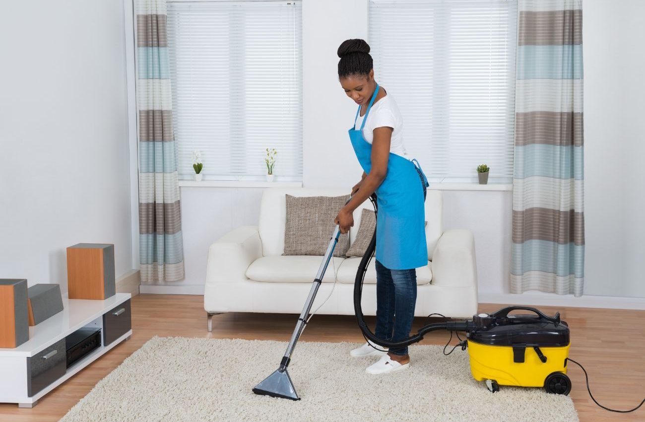 Trusted Rug Cleaning Professionals in San Antonio A woman in an apron uses a vacuum to clean a room, highlighting a rug cleaning service in San Antonio, TX.